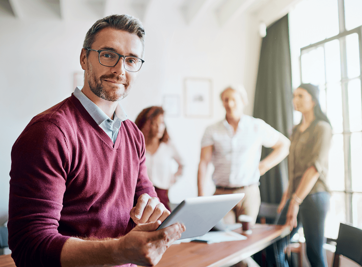 Man Holding Tablet and Smiling with Blurry People in Background