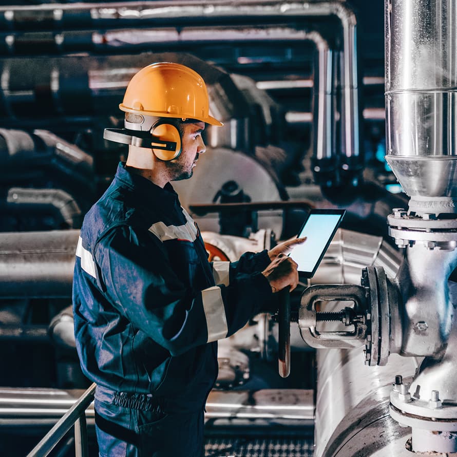 Man in Hardhat in Industrial Setting and Looking at Tablet