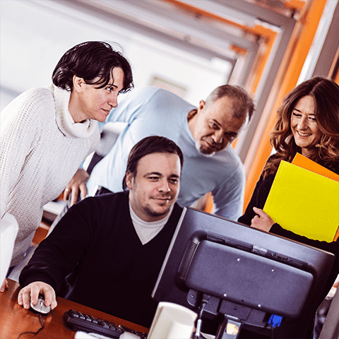Four People Gathered Around a Laptop and Smiling