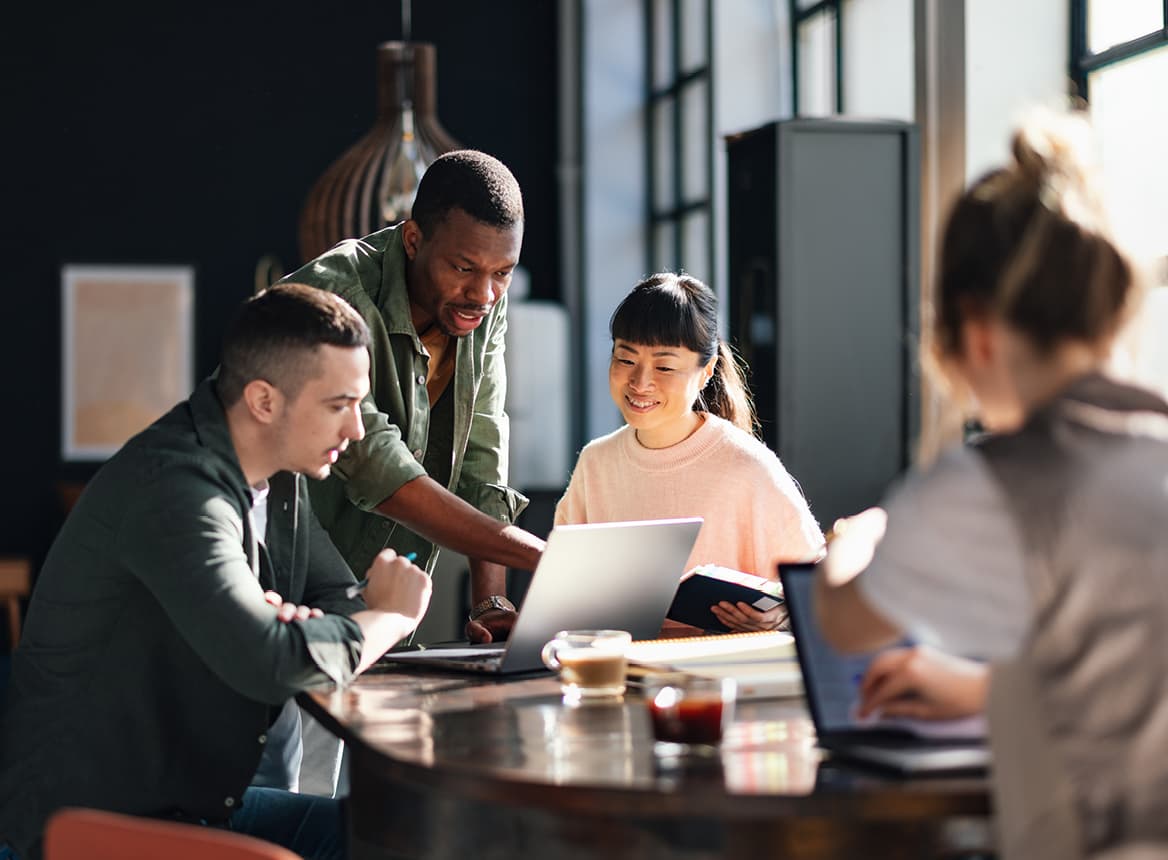 Several People Talking and Pointing Around a Laptop at a Conference Table
