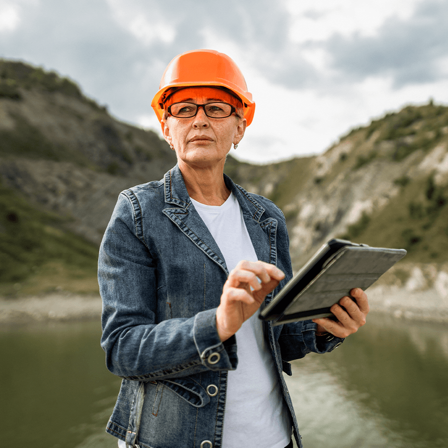 Woman Wearing Orange Hard Hat and Holding Tablet Out in Nature